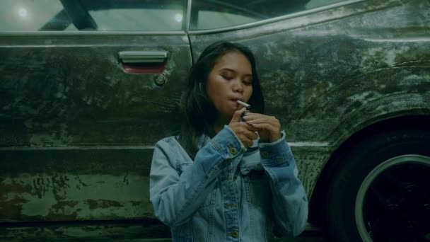 Een verdrietig thai meisje zit roken leunend tegen een roestige auto 's nachts — Stockvideo