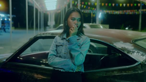 Smutna Tajka dziewczyna siedzi paląc opierając się o zardzewiały samochód w nocy — Wideo stockowe