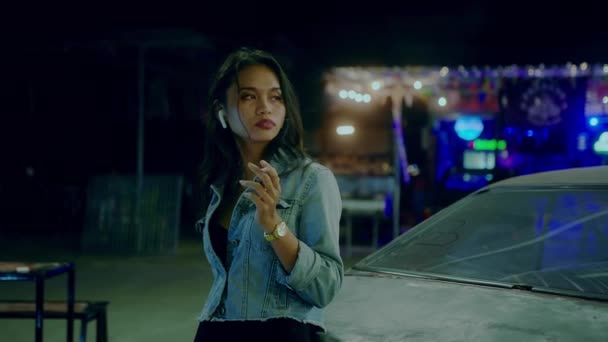 Smutna Tajka dziewczyna siedzi paląc opierając się o zardzewiały samochód w nocy — Wideo stockowe