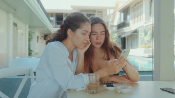 Två unga attraktiva kvinnor dricker kaffe på en restaurang och tittar på telefon — Stockvideo