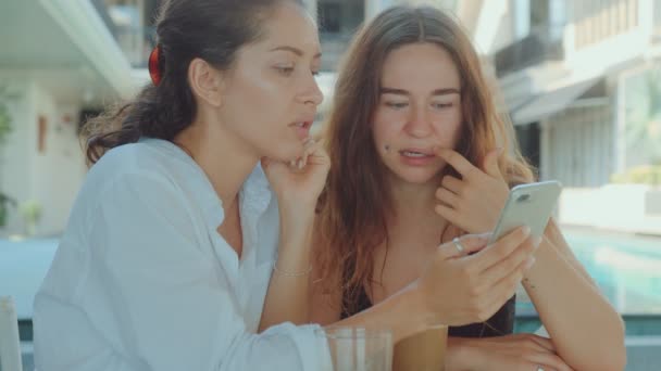 Två unga attraktiva kvinnor dricker kaffe på en restaurang och tittar på telefon — Stockvideo