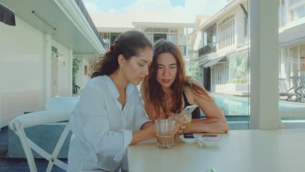 Duas jovens mulheres atraentes bebendo café em um restaurante e olhando para o telefone — Vídeo de Stock