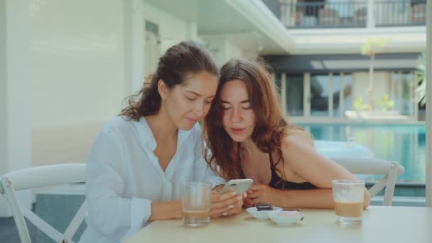 Twee mooie vrouwen lachen tijdens het gebruik van een smartphone tijdens het drinken van koffie — Stockvideo