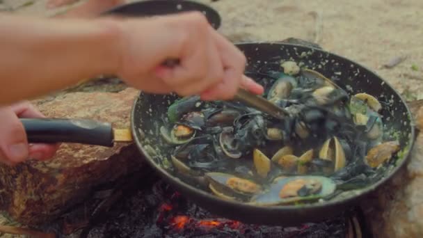 Kuchař vaří čerstvé mušle na pánvi nad ohněm na pláži. Zpomalit video s jídlem. Proces vaření italské těstoviny s mušlemi — Stock video