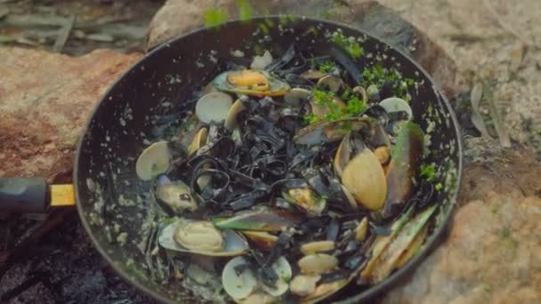 Un chef cocina mejillones frescos en una sartén sobre un fuego en la playa. Vídeo de comida en cámara lenta. Proceso de cocción de pasta italiana con mejillones — Vídeos de Stock