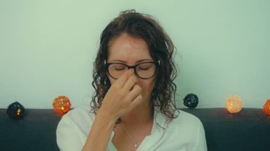 Yorgun genç bir kadın. Masaj yaparken gözlüğünü çıkarıyor. Kırmızı daire işaretli baş ağrısı