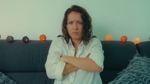 A displeased offended young woman is sitting with folded arms on sofa — Stock Video