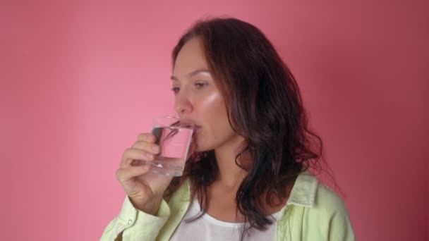 Kadın pembe arka planda bardaktan su içiyor. — Stok video