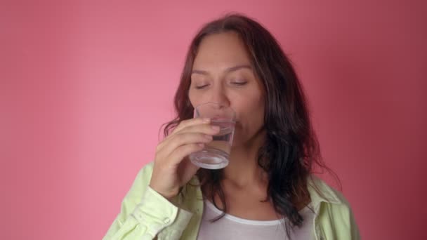 Nainen juo vettä lasista vaaleanpunaisella pohjalla — kuvapankkivideo