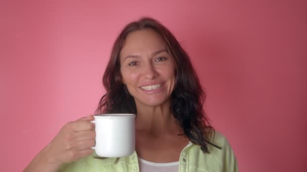 Sorridente donna allegra tenere calda tazza di caffè o tè isolato su uno sfondo di colore rosa — Video Stock