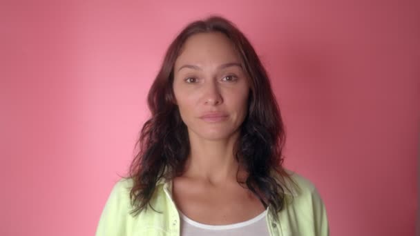 Uma mulher mostra ela é inteligente, colocando o dedo na cabeça em um fundo rosa — Vídeo de Stock
