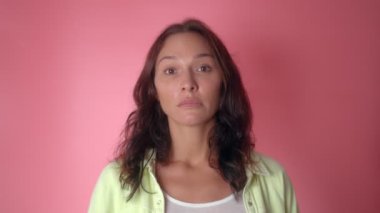 Kadın bir şeylerden şüpheleniyor, pembe arka plandaki kameraya dikkatlice bakıyor.