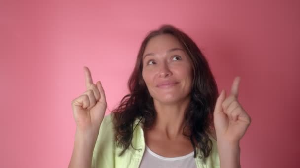 Jonge vrouw houdt handen in de lucht wijzende vingers omhoog terwijl dansen op roze achtergrond — Stockvideo