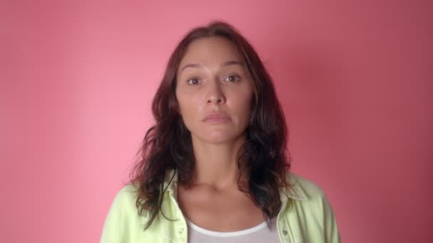 Kvinna misstänker något, tittar på kameran eftertänksamt på en rosa bakgrund — Stockvideo