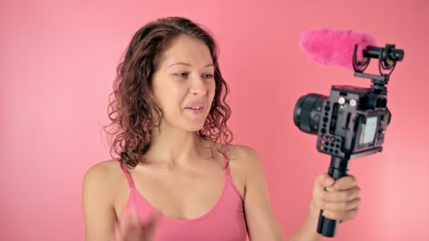 Молодая женщина vlogger запись транслируется в замедленной съемке на розовом фоне — стоковое видео