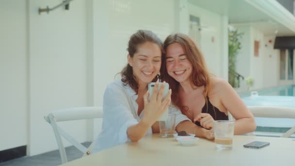 Две привлекательные девушки пьют кофе в ресторане и смотрят в телефон — стоковое видео