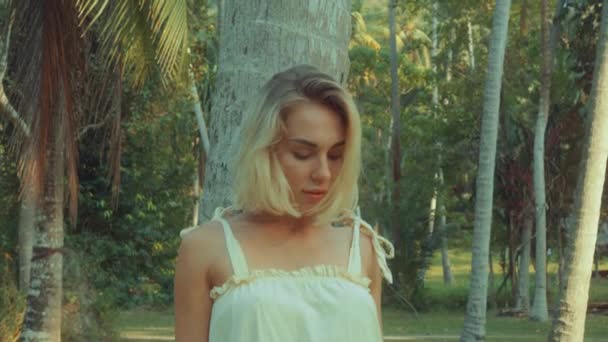 Молода блондинка стоїть, розглядаючи тропічні тропічні ліси, світло заходу сонця надходить зверху. повільне відео руху — стокове відео