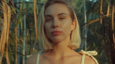 Genç sarışın, tropikal yağmur ormanlarını düşünerek ayakta duruyor, yukarıdan gün batımı ışığı geliyor. Yavaş çekim videosu