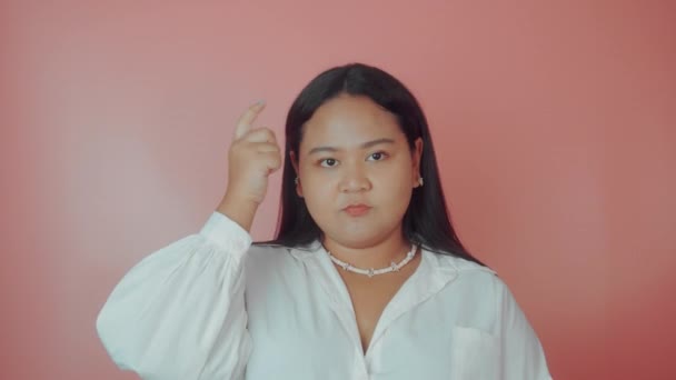 A woman shows shes clever by putting her finger to her head on a pink background — Stock Video