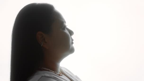 Silhouette of a woman in a white shirt looking over her shoulder at the camera — Stock Video