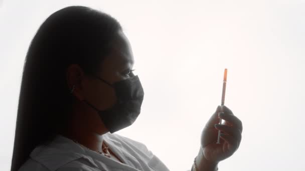 Sylwetka sporej kobiety w masce stojącej ze strzykawką — Wideo stockowe