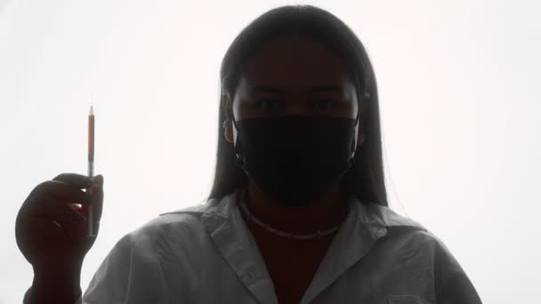 Silhuett av en stor kvinna i en mask stående med en spruta — Stockvideo
