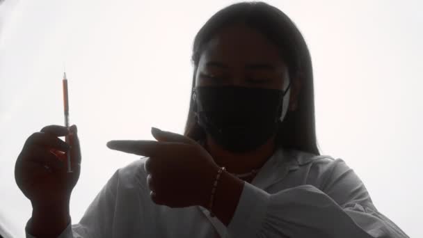 Silhouette einer ansehnlichen Frau in einer Maske, die mit einer Spritze steht — Stockvideo