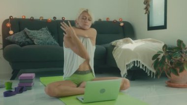 Evde dizüstü bilgisayarının önünde gerinen bir kadın. İnternetten yoga dersi alıyor.