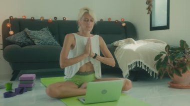 Evde dizüstü bilgisayarının önünde meditasyon yapan bir kadın. İnternetten yoga dersi alıyor.