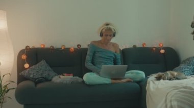 Bir kadın dizüstü bilgisayarıyla kanepede oturmuş müzik dinliyor.