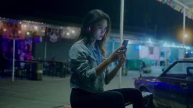 A young beautiful Asian girl on the street of a night city listening to music on her smartphone headphones