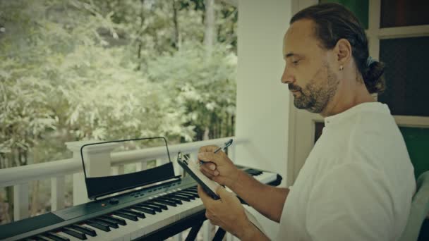 Um homem com duas mãos toca música em um instrumento de teclado. O músico é inspirado no terraço da casa. — Vídeo de Stock