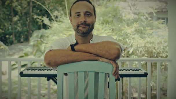 Un homme à deux mains joue de la musique sur un instrument à clavier. Le musicien s'inspire de la terrasse de la maison. — Video