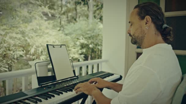 Een man met twee handen speelt muziek op een toetsenbord. De muzikant is geïnspireerd op het terras van het huis. — Stockvideo