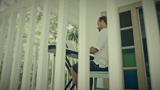 Ein Mann mit zwei Händen spielt Musik auf einem Tasteninstrument. Der Musiker lässt sich auf der Terrasse des Hauses inspirieren. — Stockvideo