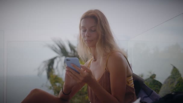 Блондинка використовує свій мобільний телефон під час відпочинку на сонці біля басейну — стокове відео
