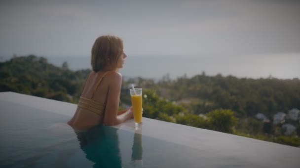 Μια ξανθιά γυναίκα πίνει mango shake ενώ χαλαρώνει στον ήλιο δίπλα στην πισίνα για διακοπές. Κομψή νεαρή γυναίκα πίνει κοκτέιλ δίπλα στην πισίνα σε αργή κίνηση. — Αρχείο Βίντεο