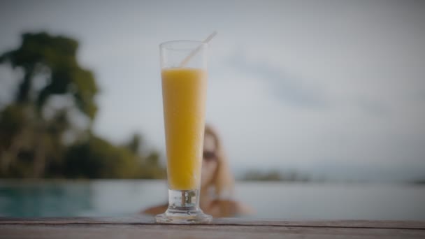 Блондинка пьет манговый коктейль, сидя на солнце у бассейна в отпуске. Элегантная молодая женщина пьет коктейль у бассейна в замедленной съемке. — стоковое видео