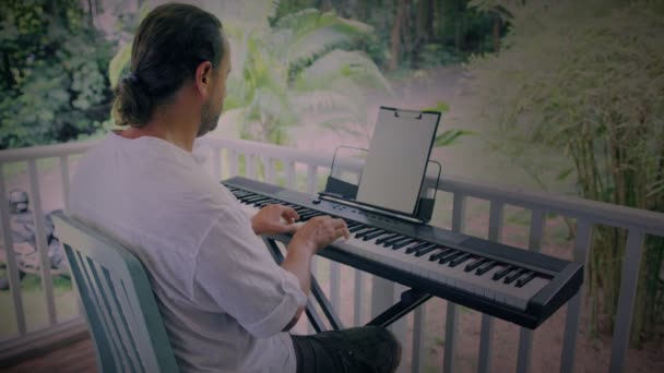 Um homem com duas mãos toca música em um instrumento de teclado. O músico é inspirado no terraço da casa. — Vídeo de Stock