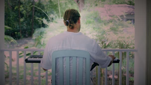 Un homme à deux mains joue de la musique sur un instrument à clavier. Le musicien s'inspire de la terrasse de la maison. — Video