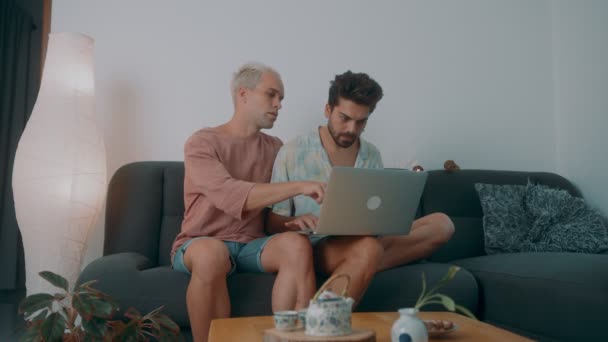 Un couple gay européen passe du temps à la maison. Ils sont allongés sur le canapé et utilisent leur ordinateur portable. — Video