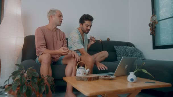 Les hommes LGBTQ regardent ensemble un film sur Internet alors qu'ils sont assis sur un canapé et boivent du thé — Video