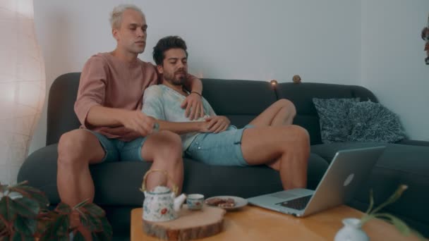 ソファに座ってお茶を飲みながらインターネットで映画を見ているLGBTQの男性 — ストック動画