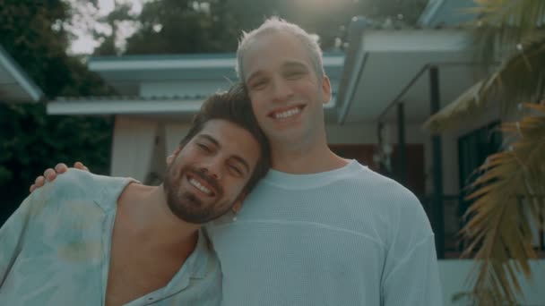 Um jovem casal gay compra uma casa nova. Homens gays felizes abraçam-se na frente de sua casa recém-comprada. Clientes entusiasmados comprando uma propriedade ou um apartamento. — Vídeo de Stock