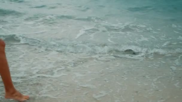 Une blonde mince en robe jaune se promène le long de la plage et regarde autour de lui — Video