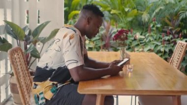 Genç Afro-Amerikalı adam kahve dükkanında akıllı telefon kullanıyor.