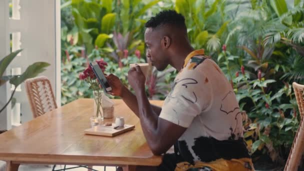 Young African-American man uses smartphone in coffee shop — Stock Video