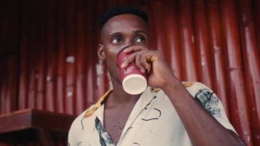 Afro-Amerikalı bir adam kahve dükkanında dururken gülümsüyor.