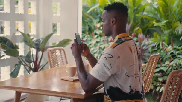 Jonge Afro-Amerikaanse man gebruikt smartphone in coffeeshop — Stockvideo