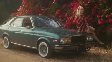Sarışın Beyaz Kadın, Teal Classic Car 'ın kaputuna tünemiş, Çiçekli Çitlere Karşı Gevşek Poz, Editör